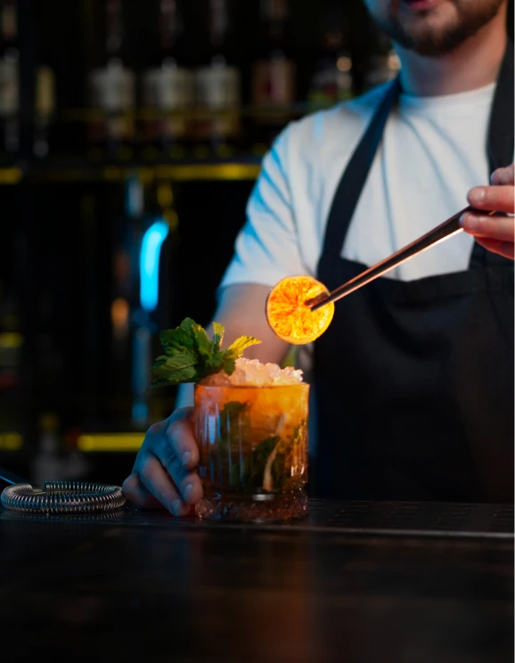Bartender decorando un c&oacute;ctel con una rodaja de naranja flameada.