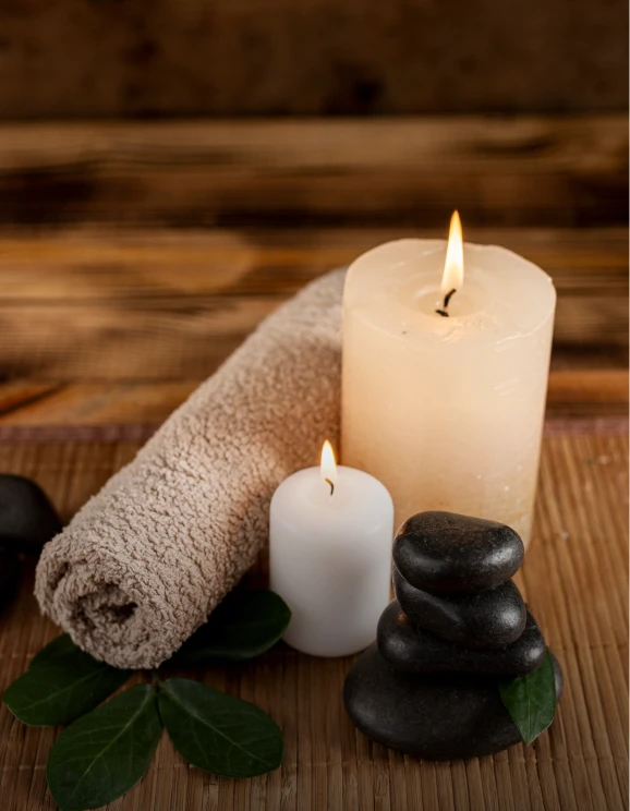 Velas encendidas, toalla enrollada y piedras sobre estera de bamb&uacute;.