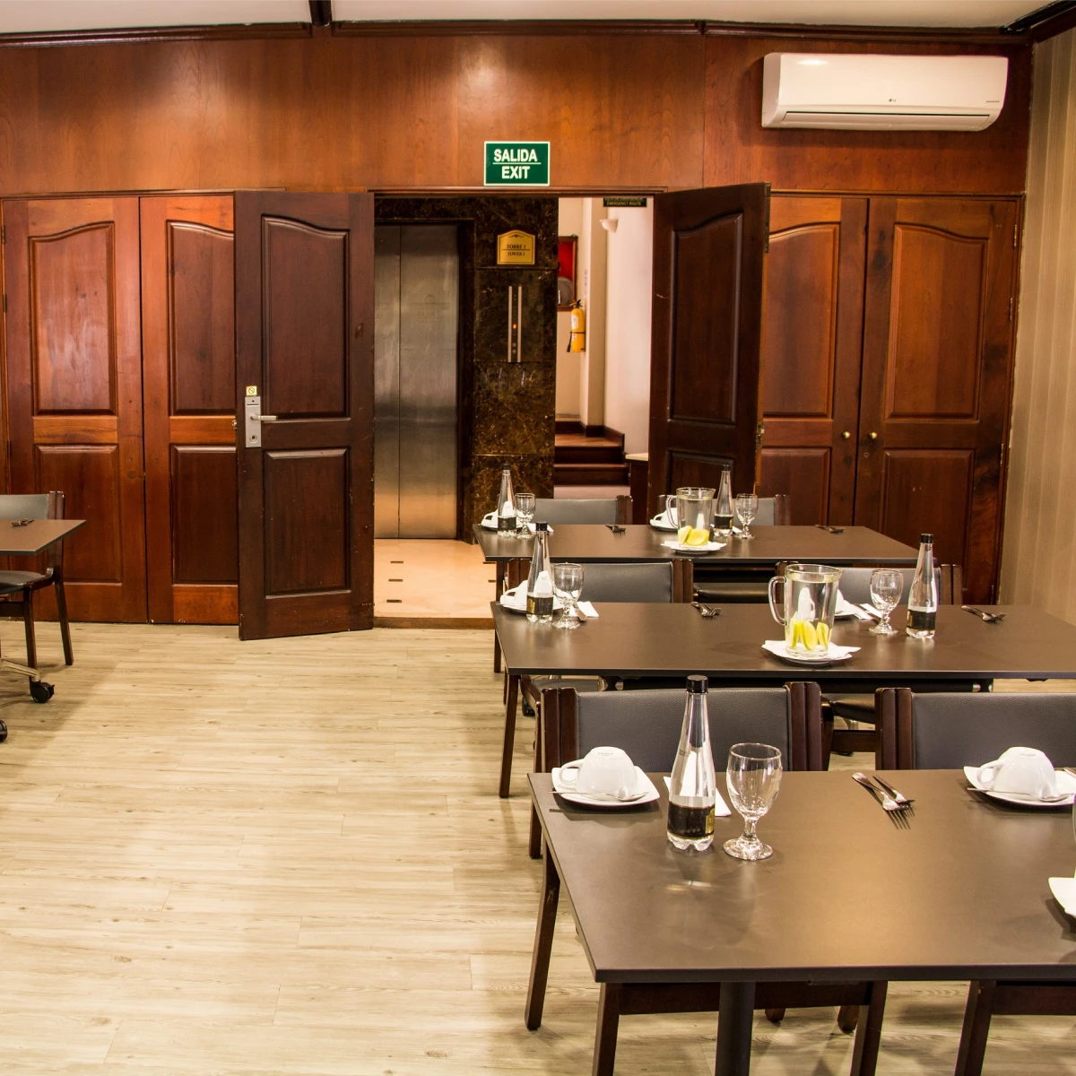 Mesas arregladas en un restaurante, puertas y un letrero de salida al fondo.