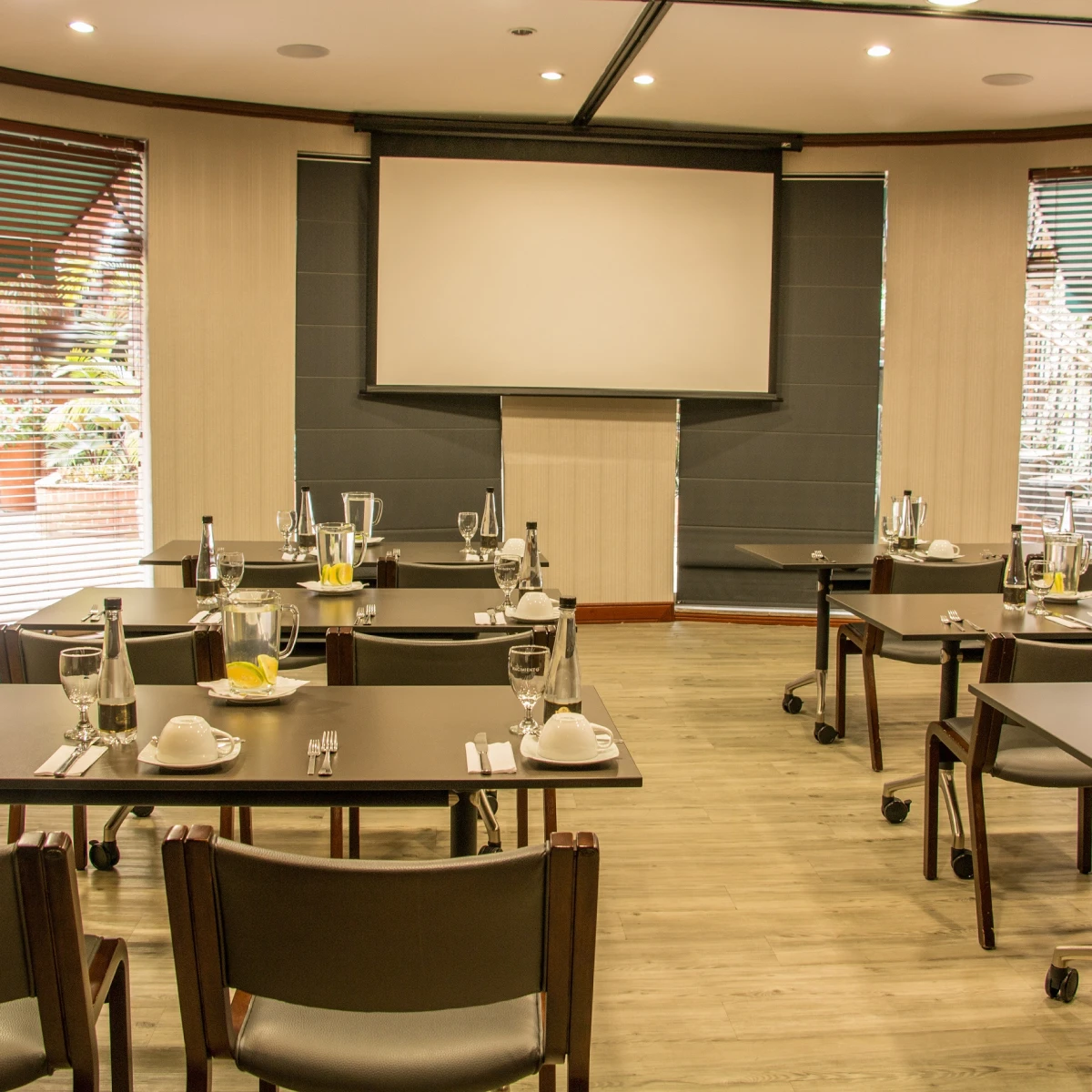 Sala de reuniones con mesas, sillas y pantalla de proyecci&oacute;n.