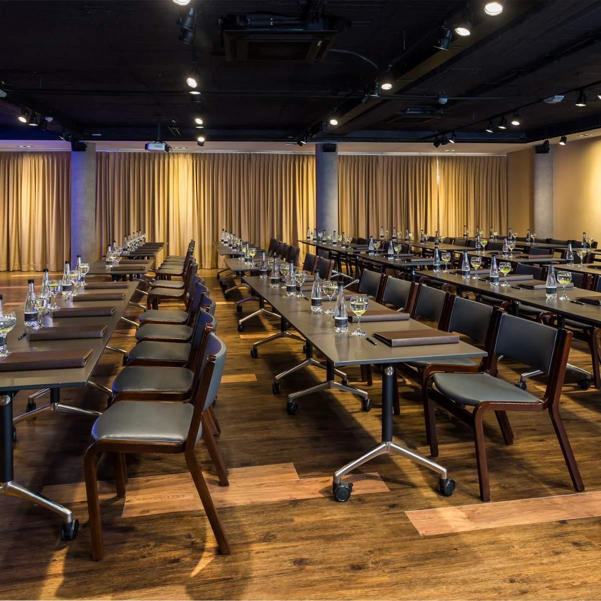 Sala de conferencias vac&iacute;a con mesas y sillas dispuestas en filas.