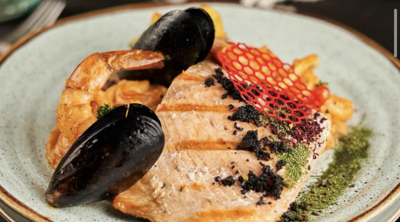 Plato gourmet con salm&oacute;n, mejill&oacute;n y camar&oacute;n decorado con especias y rejilla roja.