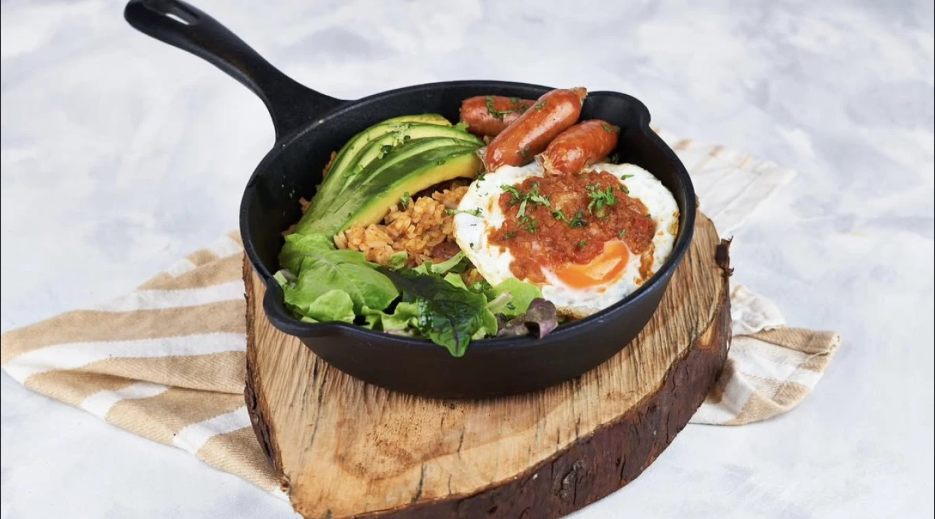 Sart&eacute;n con huevo frito, salchichas, aguacate, arroz y lechuga en rodaja de madera.