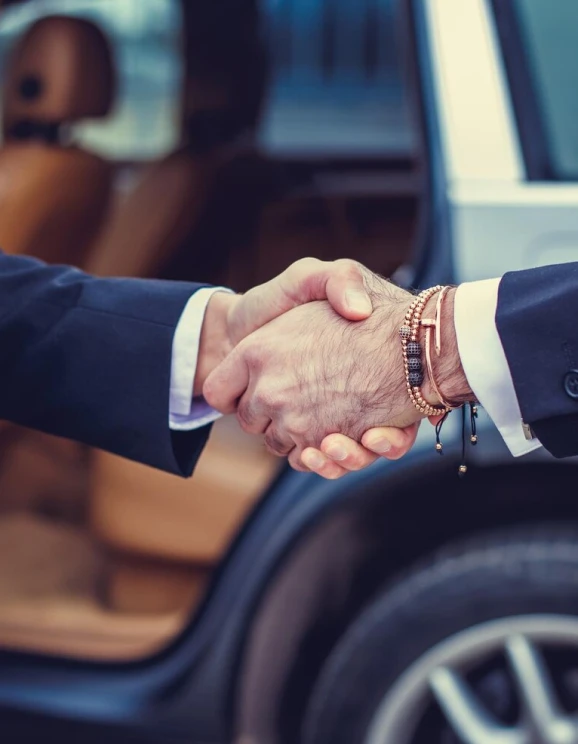 Dos personas salud&aacute;ndose de mano junto a un autom&oacute;vil.