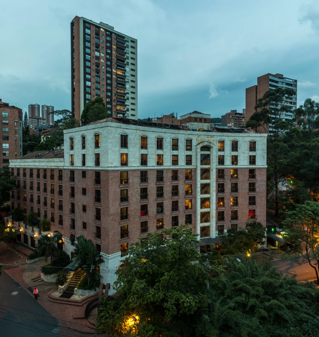 Edificio rojo al anochecer, rodeado de &aacute;rboles y otros edificios altos.