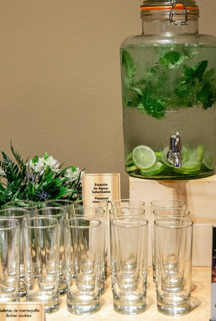 Dispenser de agua con menta y lim&oacute;n, vasos vac&iacute;os delante sobre la mesa.