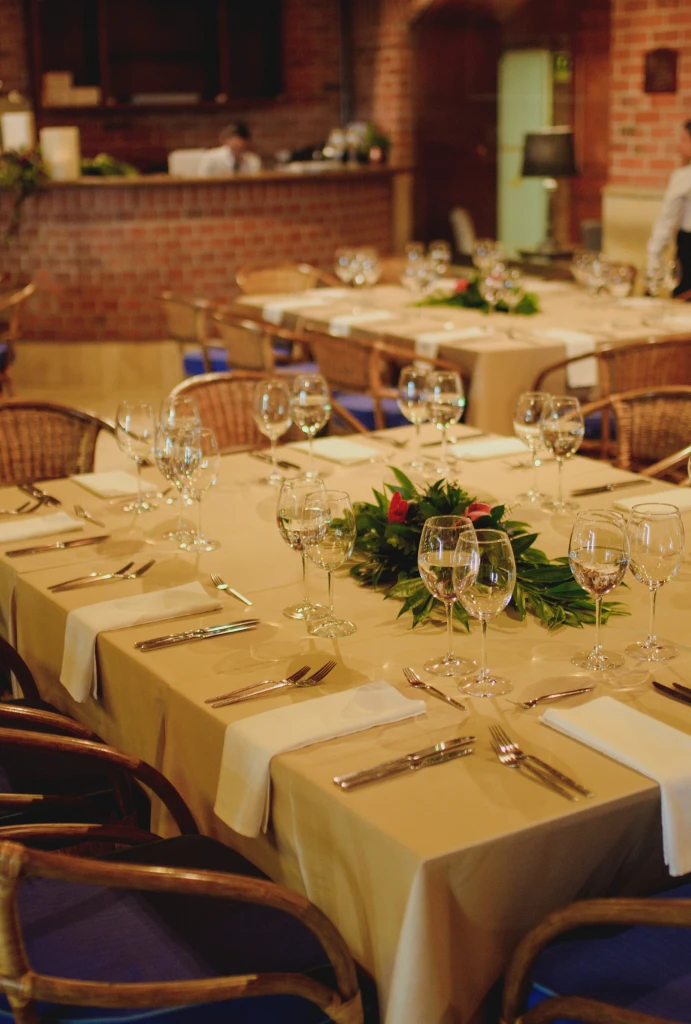 Mesa elegante con cubiertos y copas, rodeada de sillas, decoraci&oacute;n central verde.