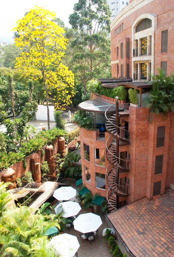 Edificio de ladrillo con escaleras espirales y jard&iacute;n con sombrillas blancas.