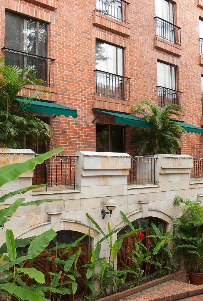 Edificio de ladrillo con balcones, ventanas y plantas alrededor.