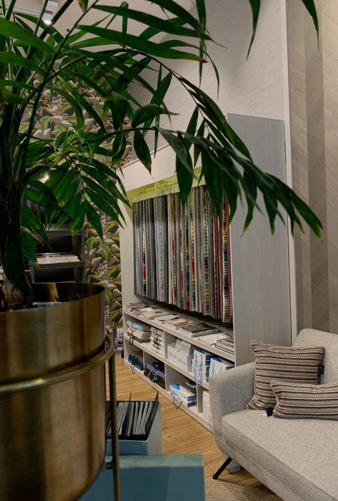 Planta en maceta dorada junto a estanter&iacute;a y sof&aacute; con cojines.