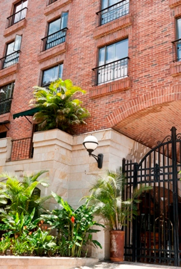 Edificio de ladrillo con ventanas y plantas en la entrada con una reja negra.