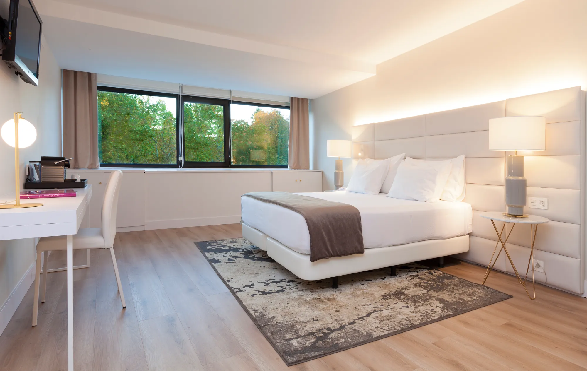 Habitaci&oacute;n moderna con cama doble, escritorio y ventana con vista al exterior.