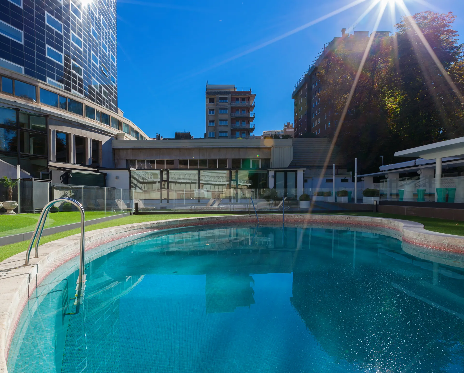 Piscina al aire libre con edificios y sol brillante al fondo.
