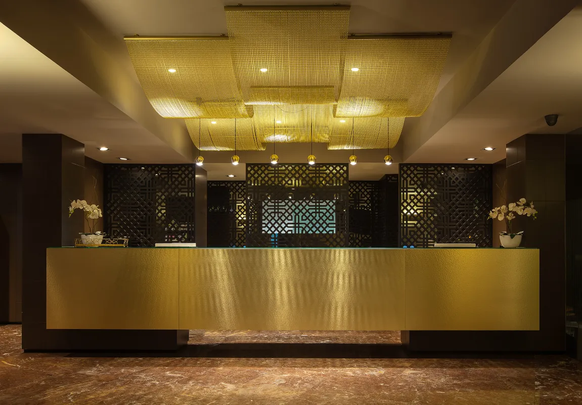 Recepci&oacute;n de hotel moderna con mostrador dorado y luces c&aacute;lidas.
