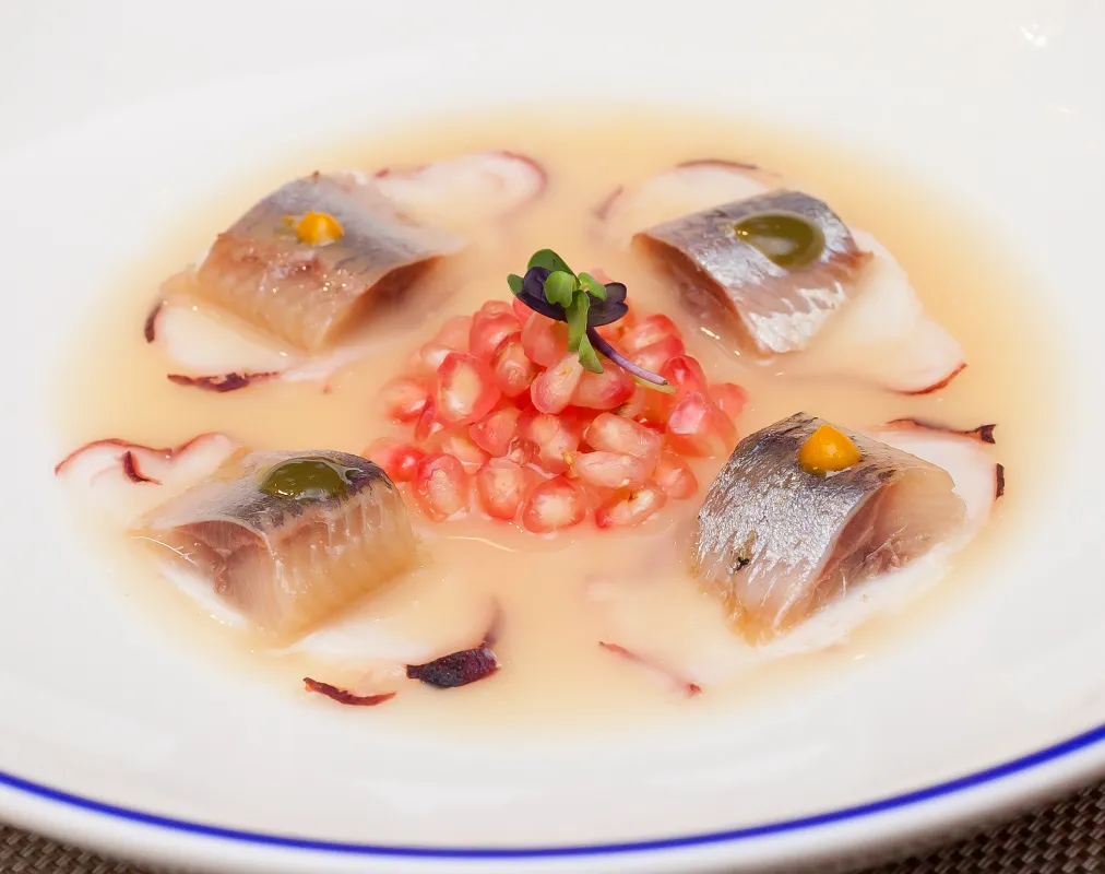 Plato con mariscos, granada y brotes verdes en caldo claro.