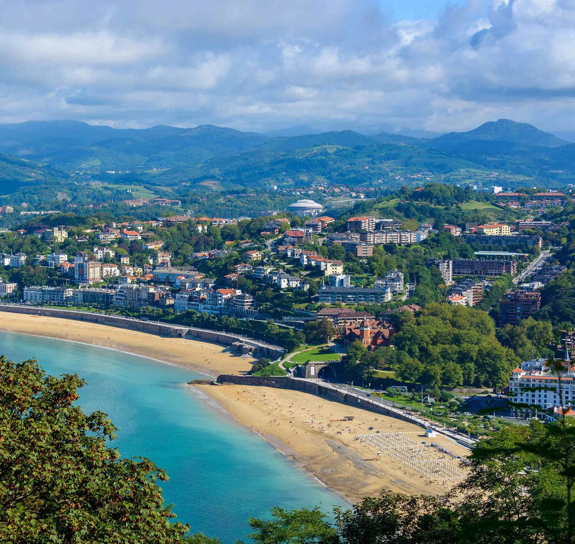 Vista panor&aacute;mica de una playa con ciudad y monta&ntilde;as al fondo.