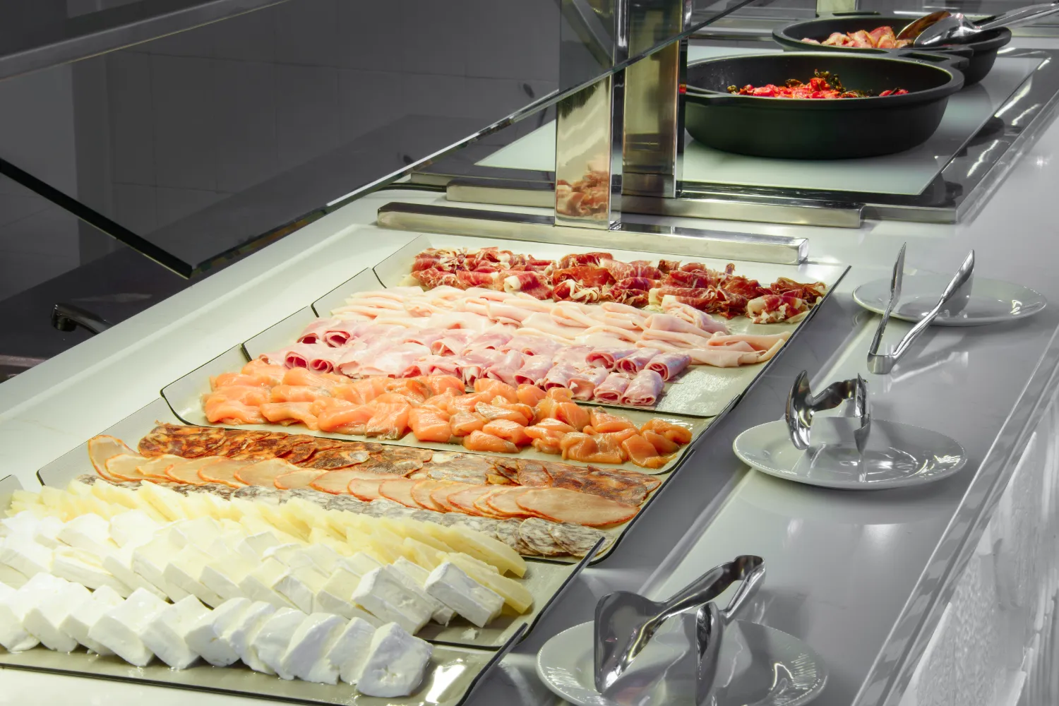 Buffet de charcuter&iacute;a y queso con pinzas y platos.