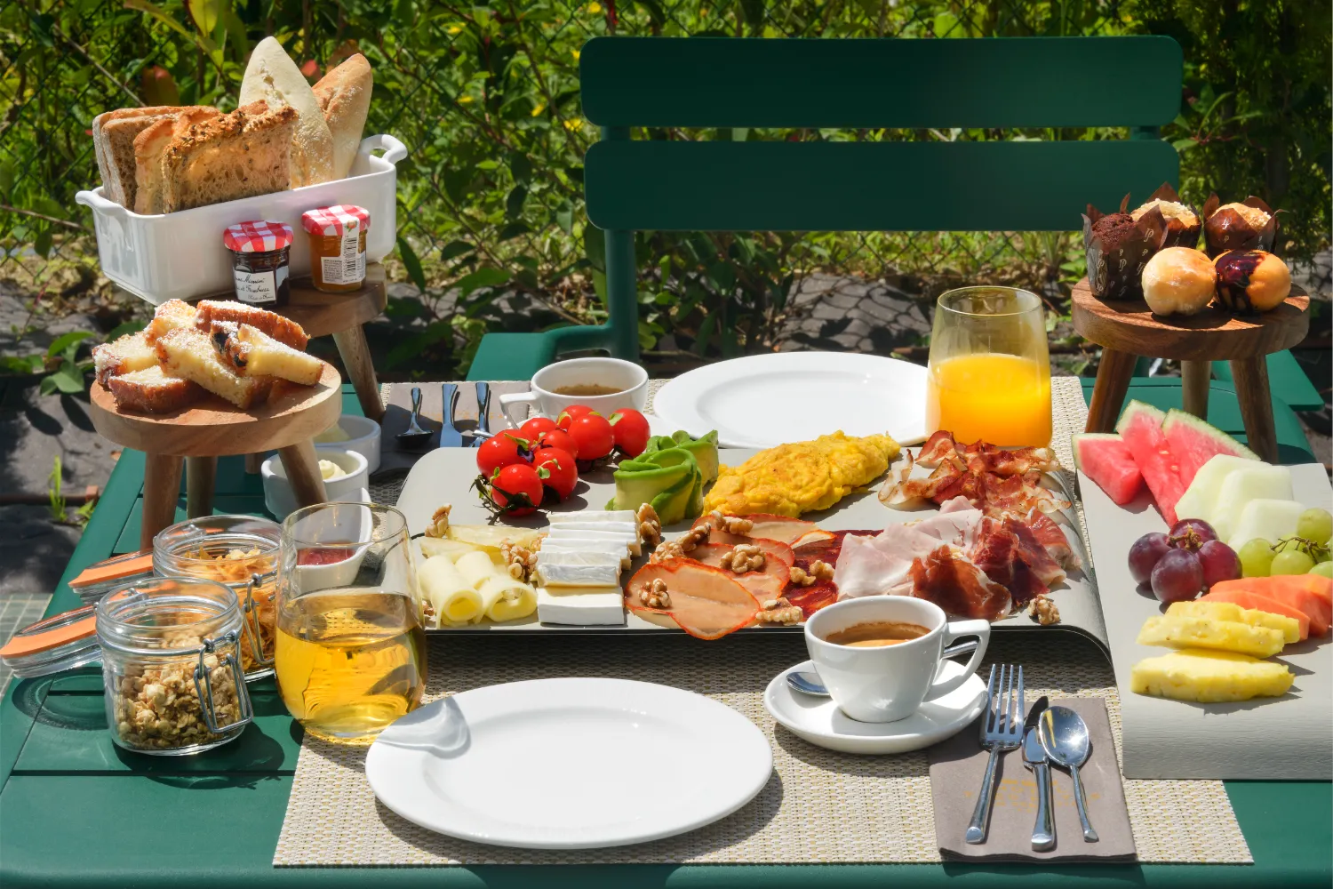 Desayuno variado al aire libre con frutas, panes, quesos, jam&oacute;n y caf&eacute;.