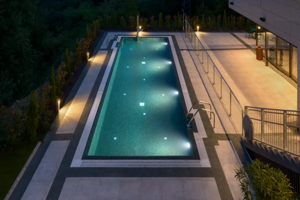 Piscina iluminada por la noche junto a una terraza con barandillas.