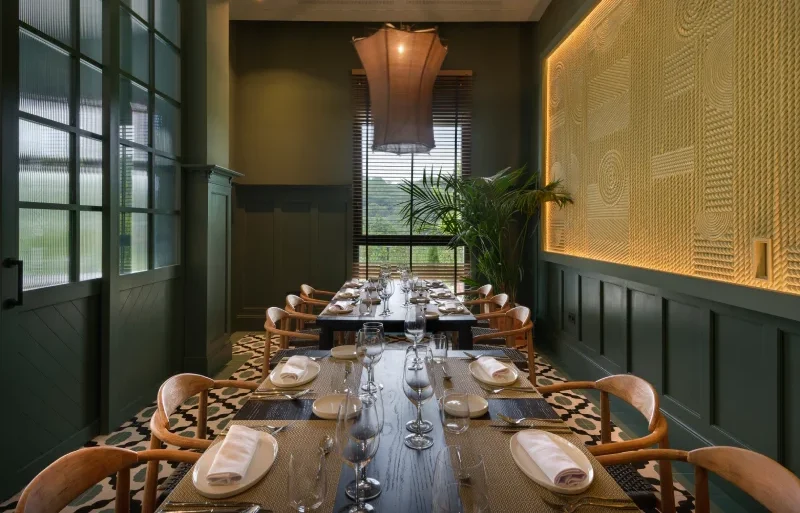 Comedor elegante con mesa servida, decoraci&oacute;n verde y luz suave.