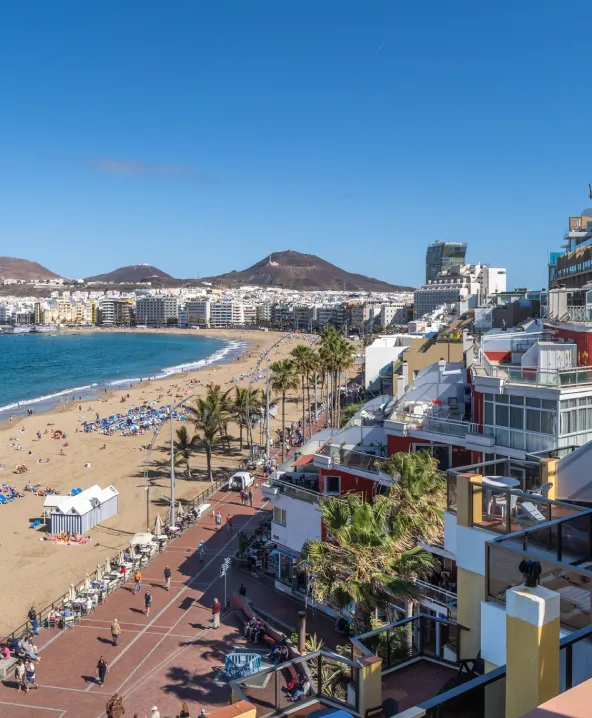Playa soleada con edificios y paseo mar&iacute;timo lleno de gente.