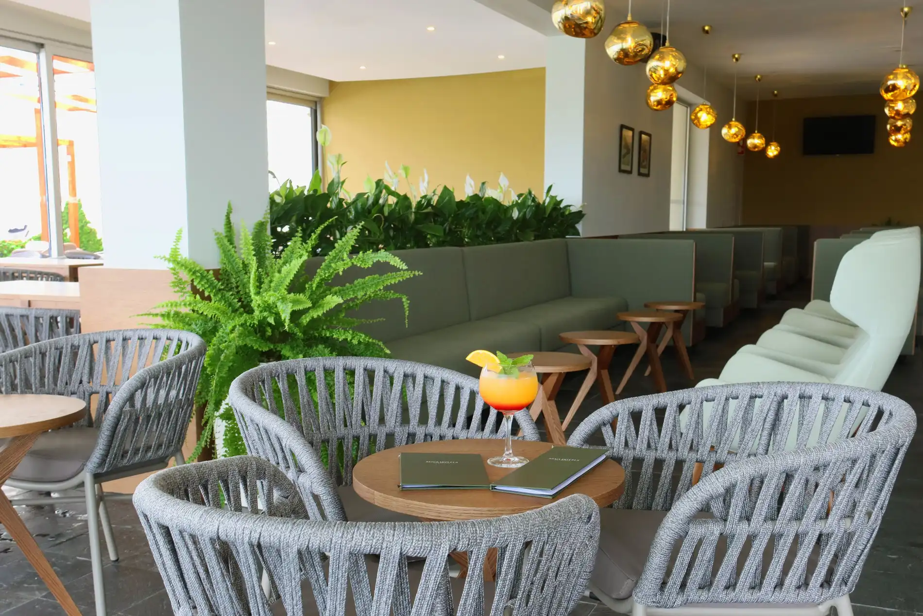 Lounge moderno com poltronas, mesas e lumin&aacute;rias douradas pendentes.