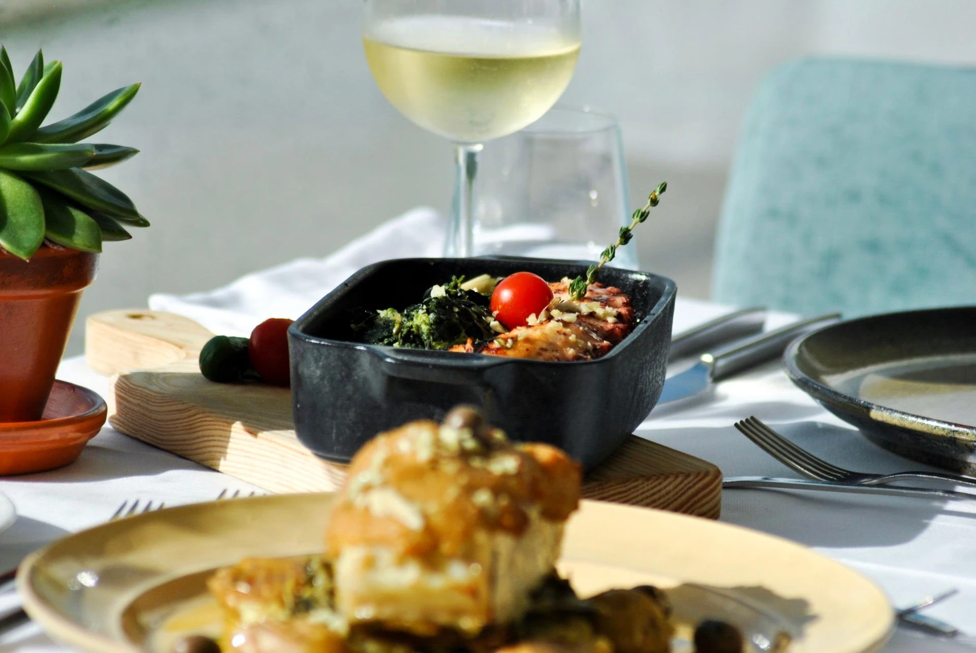 Prato de comida decorado com ta&ccedil;a de vinho branco ao fundo.