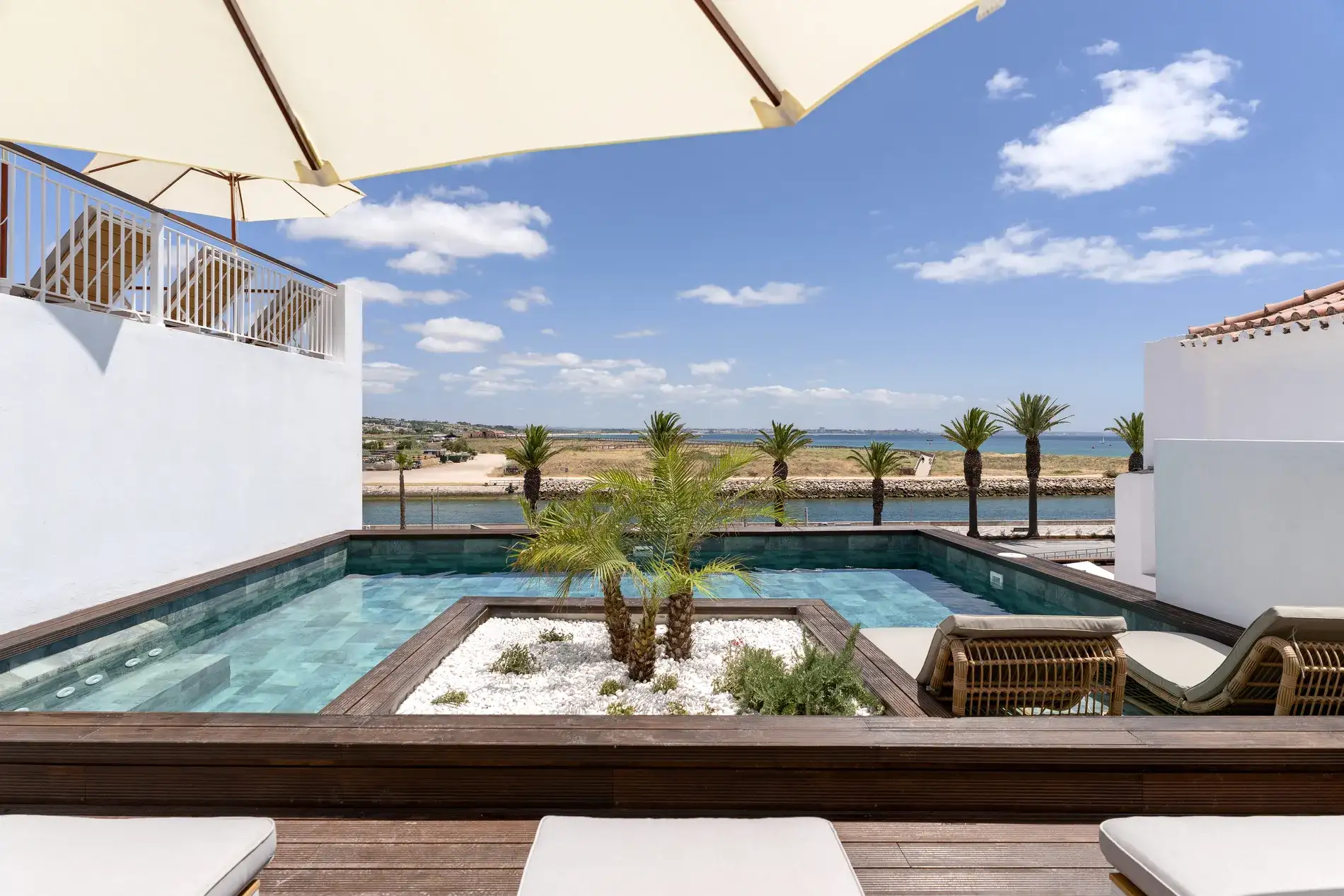 Piscina com vista para palmeiras e mar sob c&eacute;u azul claro.