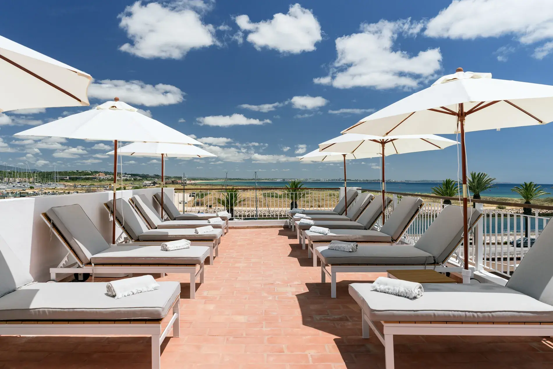 Espregui&ccedil;adeiras e guarda-s&oacute;is em terra&ccedil;o &agrave; beira-mar, c&eacute;u azul ao fundo.