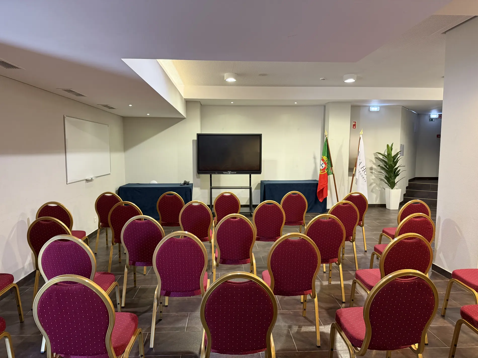 Sala de confer&ecirc;ncias com cadeiras vermelhas e tela ao fundo.