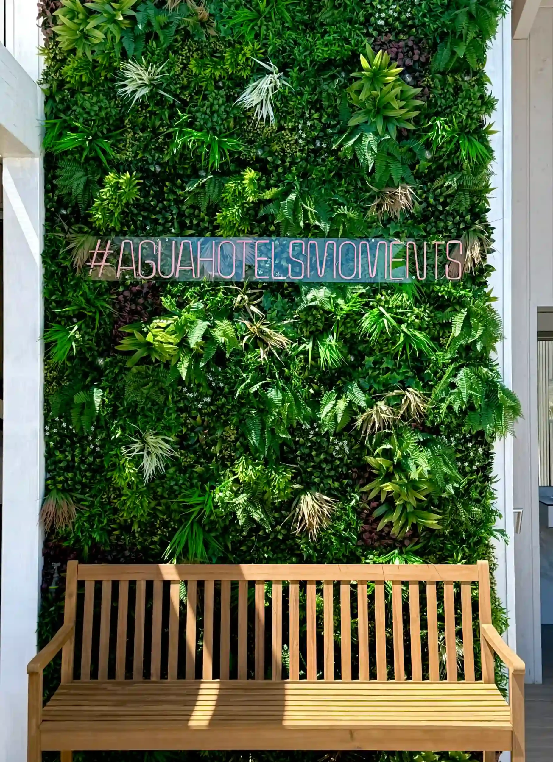 Parede verde com banco e hashtag: #AGUAHOTELSMOMENTS.