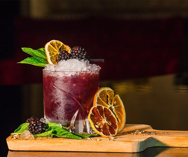 Coquetel decorado com amoras, folhas de hortel&atilde; e fatias de laranja desidratada.