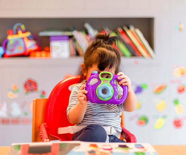Crian&ccedil;a segurando c&acirc;mera de brinquedo em sala colorida.