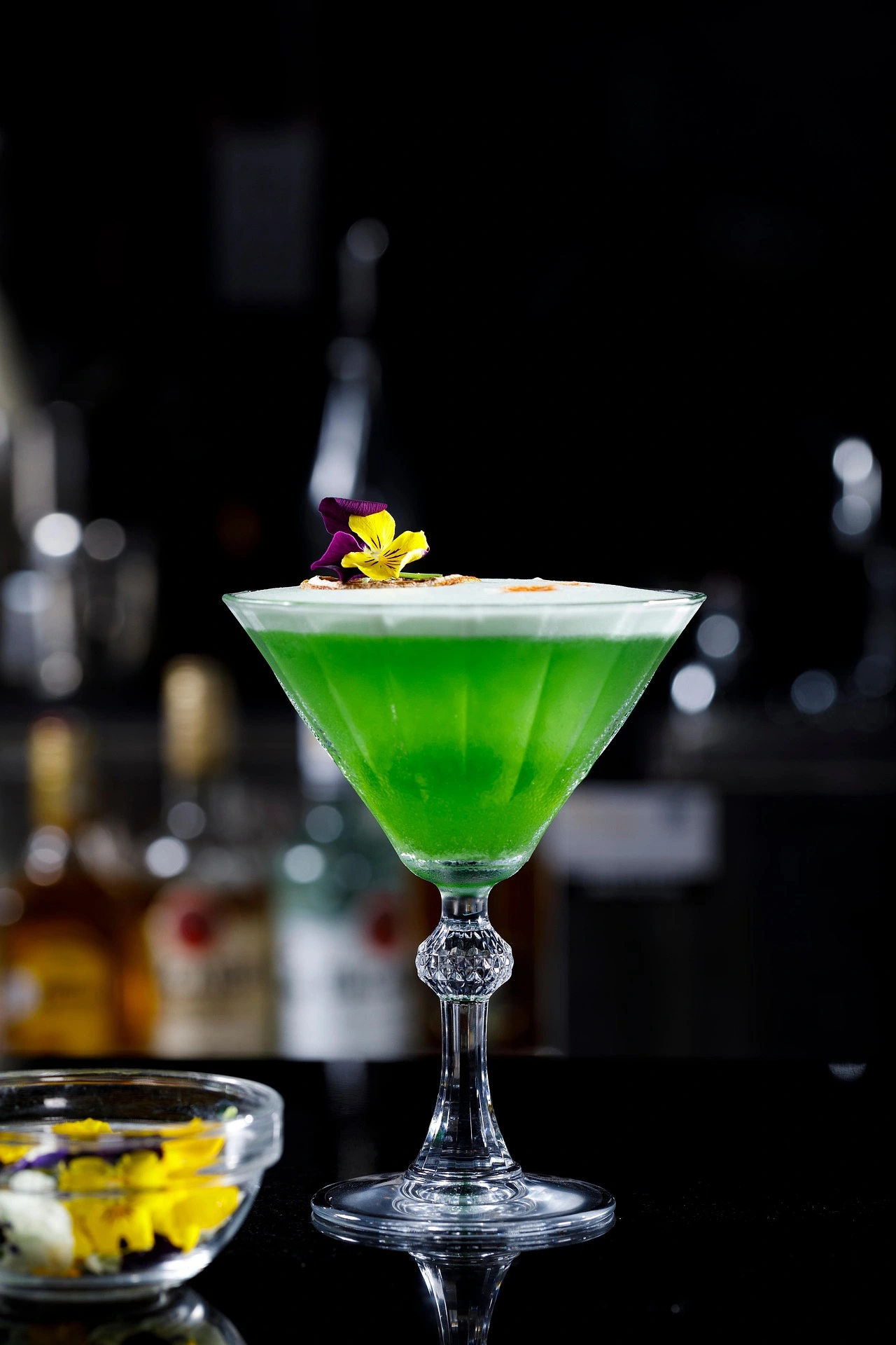 Coquetel verde em ta&ccedil;a decorado com flores coloridas.