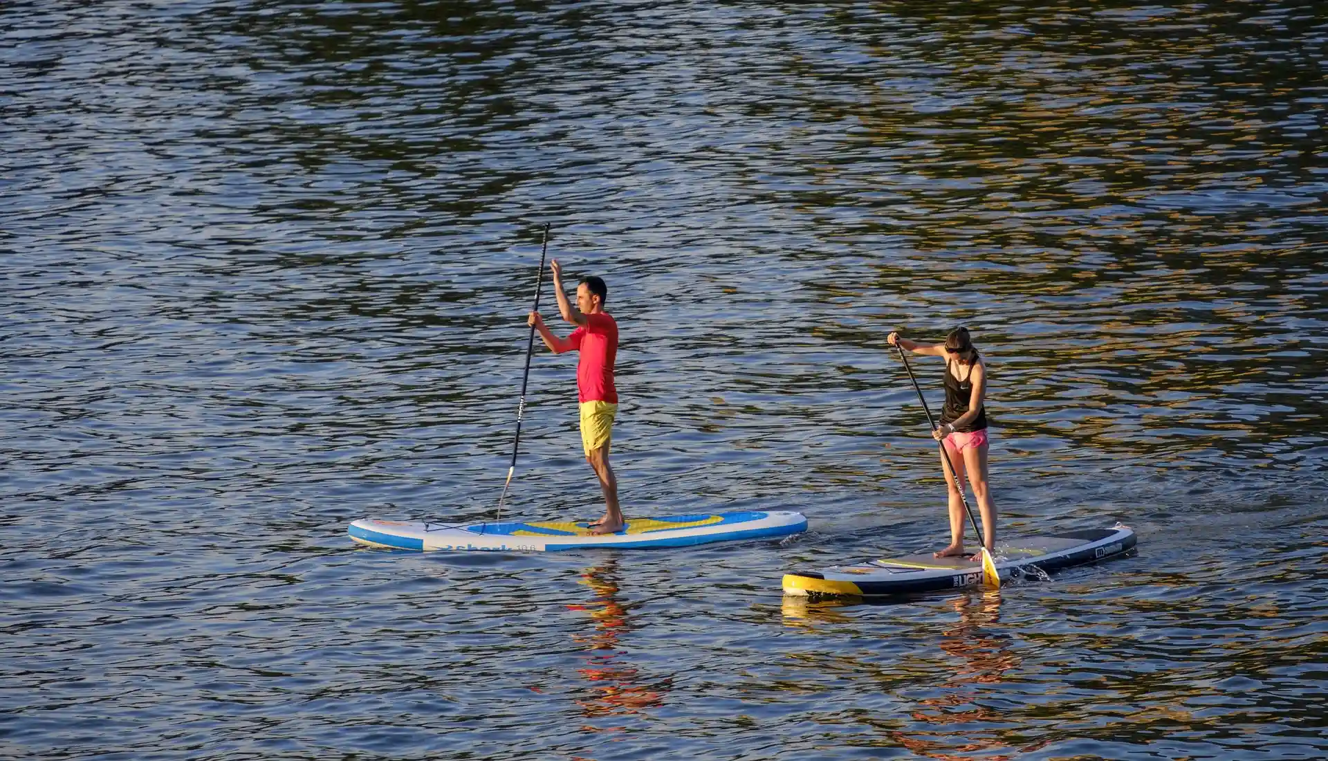 Duas pessoas praticando stand up paddle em um corpo d'&aacute;gua.