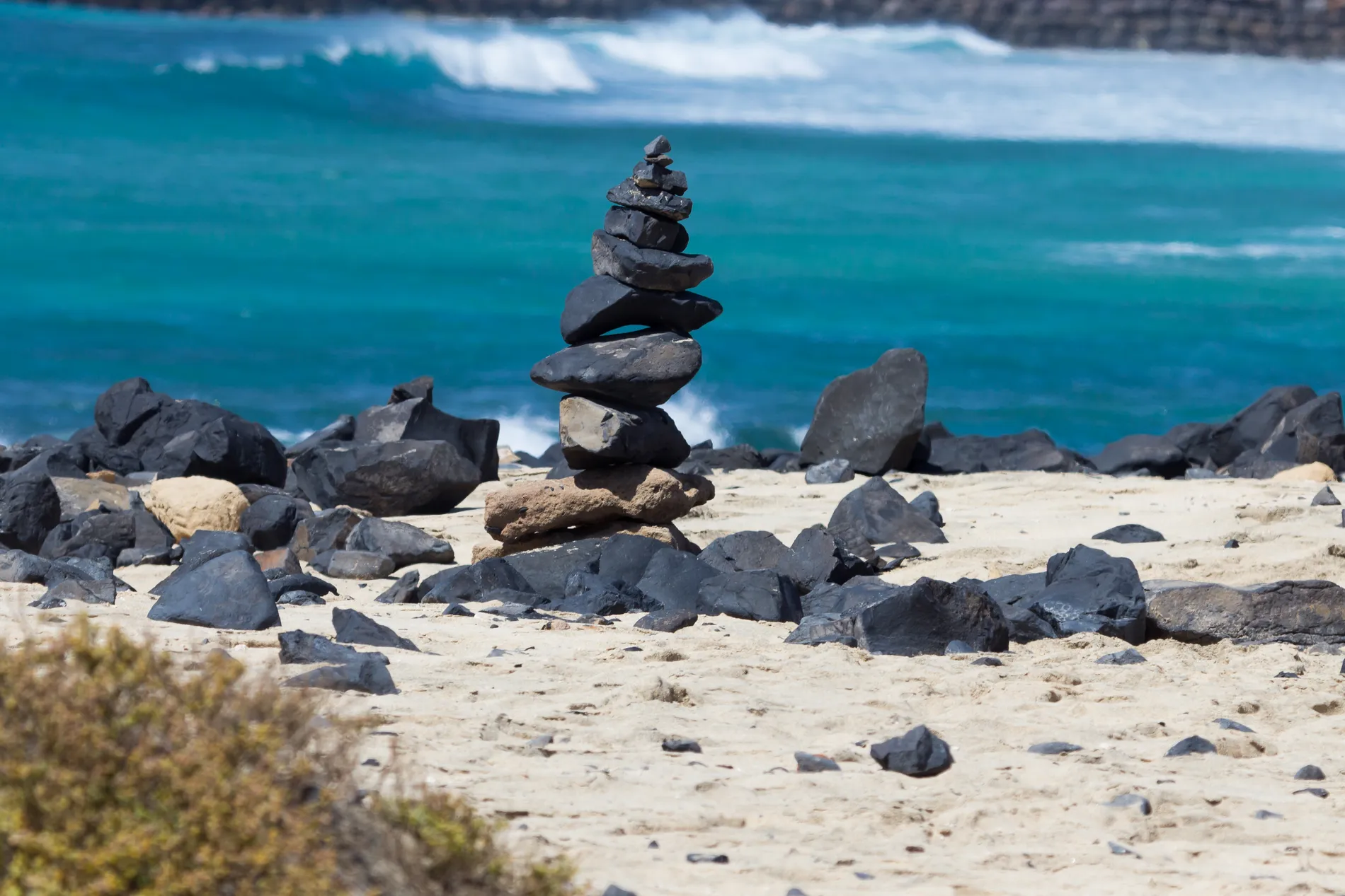Pilhas de pedras equilibradas na praia com ondas ao fundo.