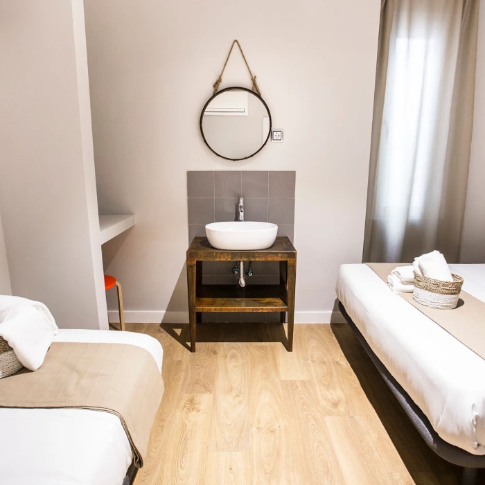 Habitaci&oacute;n moderna con camas, lavabo de madera y espejo redondo.