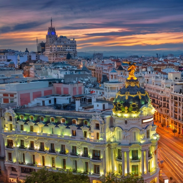 Edificios iluminados al atardecer en una ciudad con cielo colorido en el fondo.