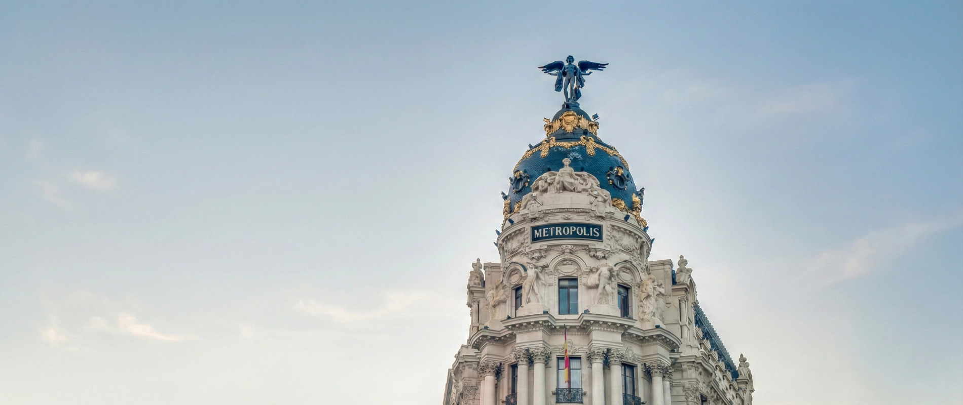 Edificio Metr&oacute;polis con c&uacute;pula azul y estatua en Madrid, cielo despejado.