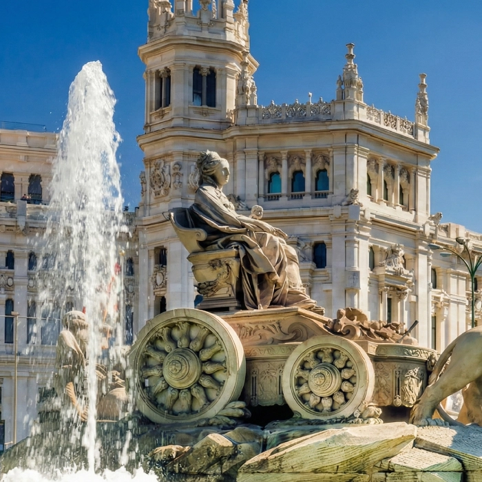 Fuente de Cibeles en Madrid con edificio hist&oacute;rico de fondo, cielos despejados.