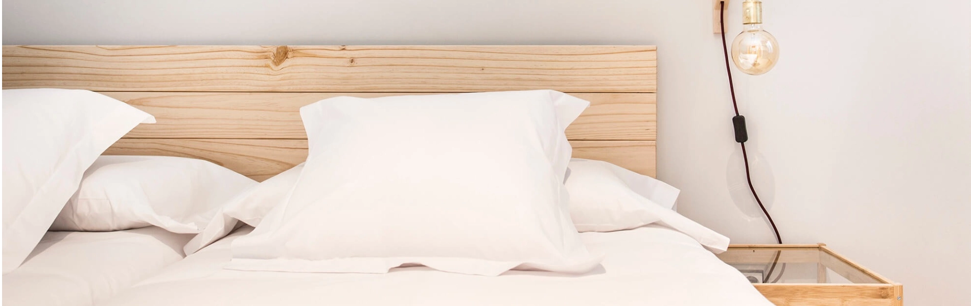 Cama con cabecera de madera, luz colgante y almohadas blancas.