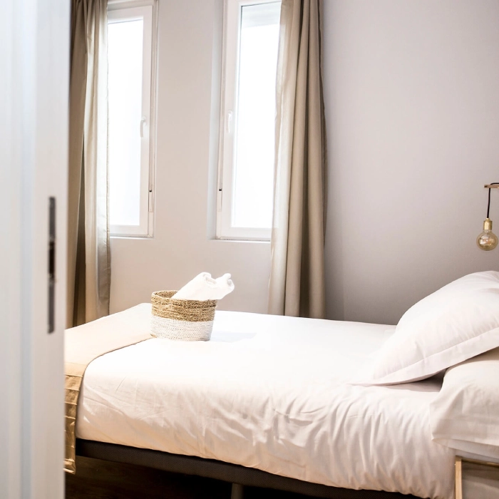 Habitaci&oacute;n iluminada con cama blanca y cesto de toallas blancas.