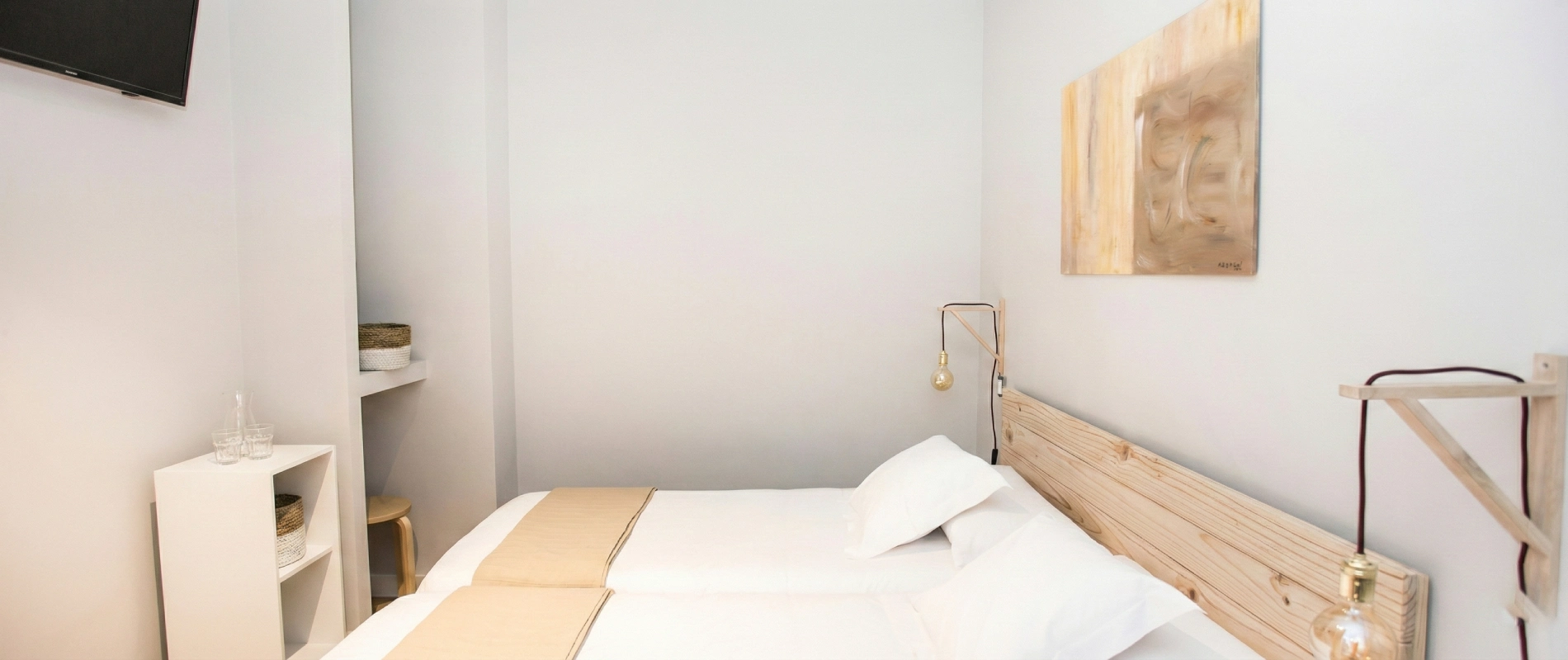 Cuarto minimalista con cama doble, l&aacute;mpara colgante y TV en la pared.