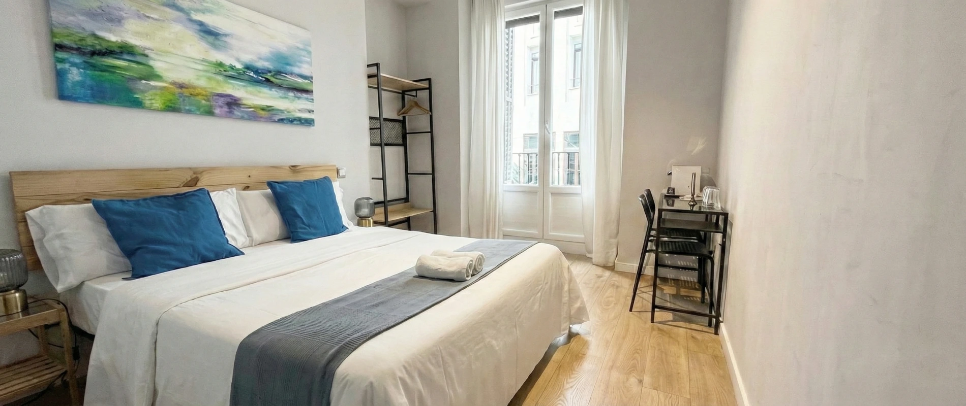 Dormitorio moderno con cama doble, escritorio y ventana grande.