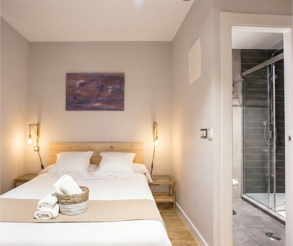 Habitaci&oacute;n moderna con cama doble, l&aacute;mparas colgantes y ba&ntilde;o con ducha.