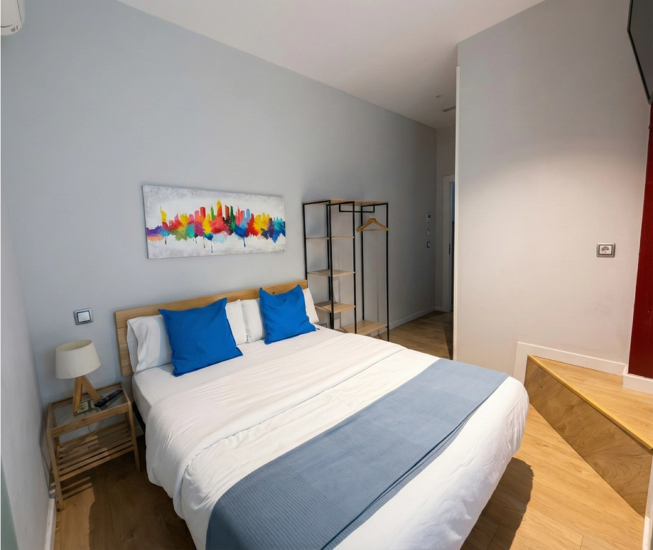 Habitaci&oacute;n con cama doble, cojines azules y pintura colorida en la pared.