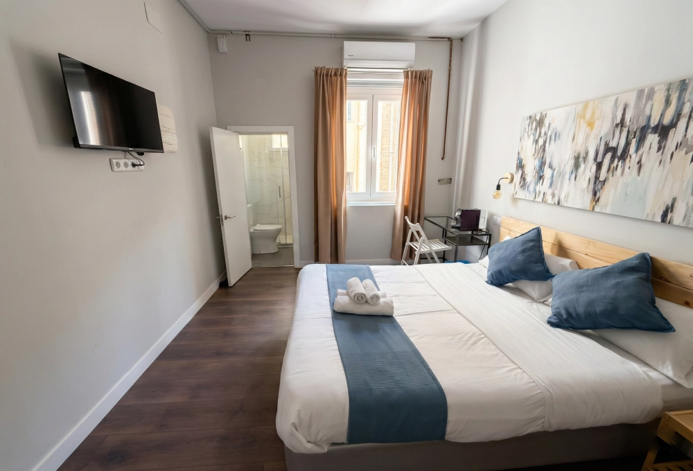 Habitaci&oacute;n moderna con cama doble, televisor y ba&ntilde;o al fondo.