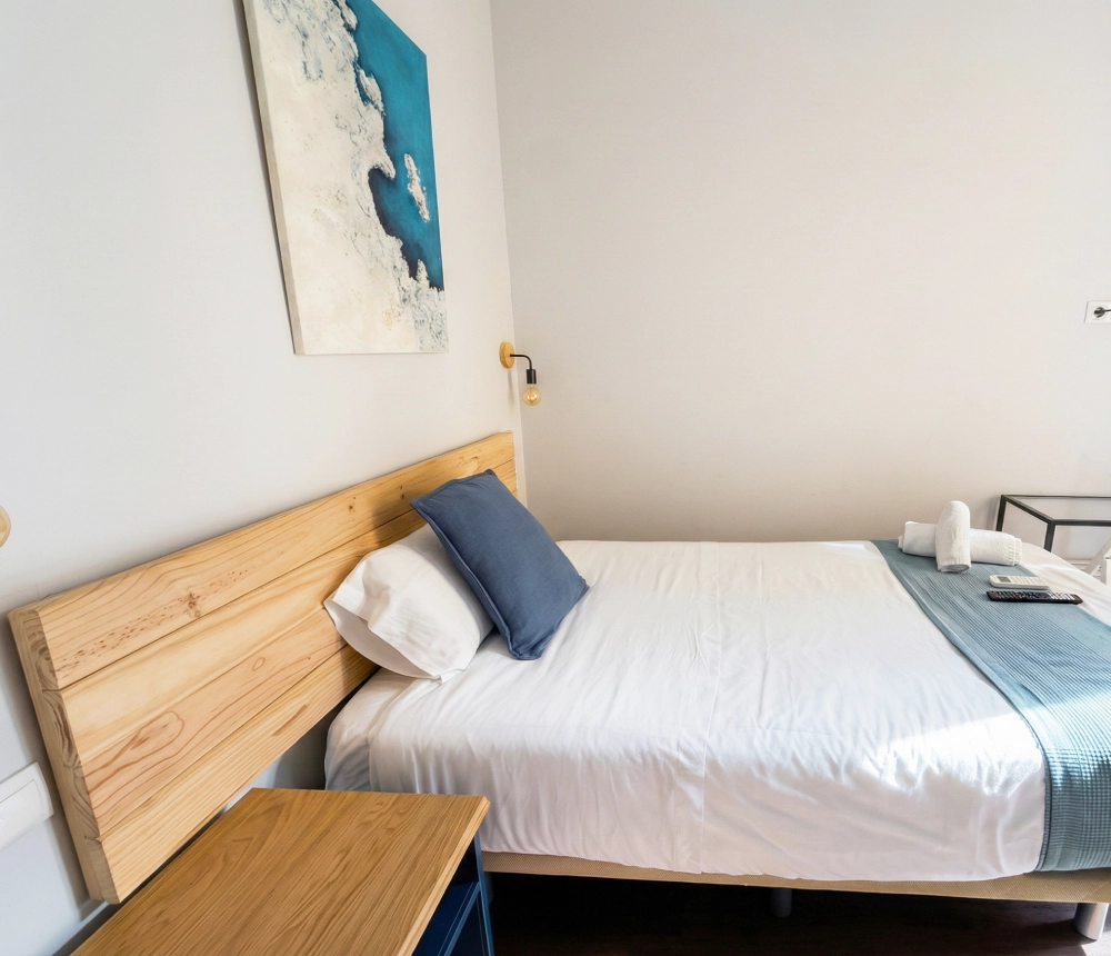 Habitaci&oacute;n minimalista con cama, cuadros y mesita.