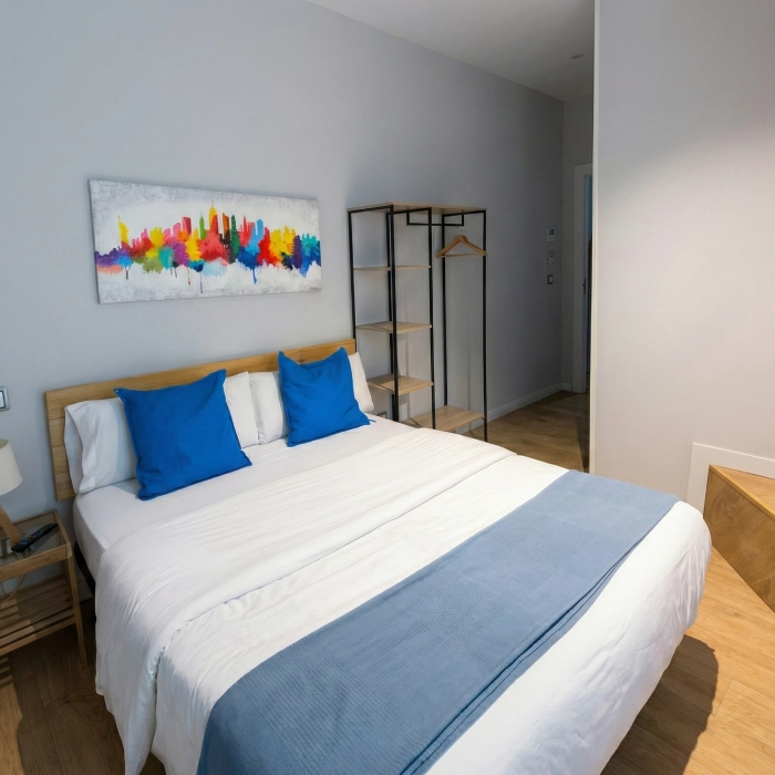 Habitaci&oacute;n moderna con cama, cojines azules y arte colorido en la pared.