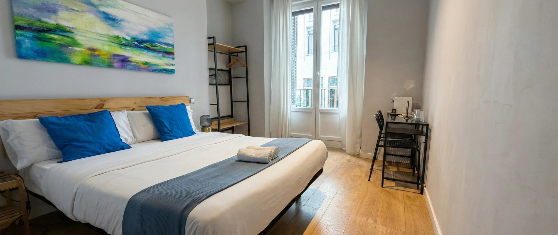 Habitaci&oacute;n moderna con cama, escritorio y ventana grande con cortinas blancas.